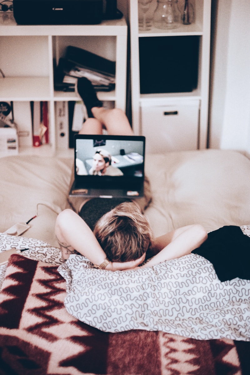 woman lying on bed while watching tv